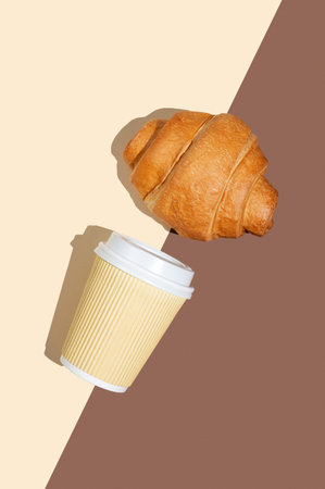 Paper cup with coffee and fresh croissant on yellow and brown background. Creative mockup for cafe menu advertising and fast breakfast concept. Top view and copy space.の写真素材