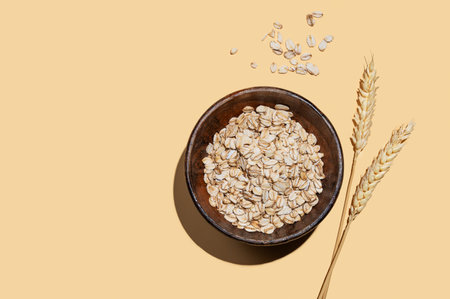 Oat flakes in a wooden bowl with wheat on a yellow background with shadow. Healthy eating and wholesome diet breakfast concept. Top view and copy space.の写真素材