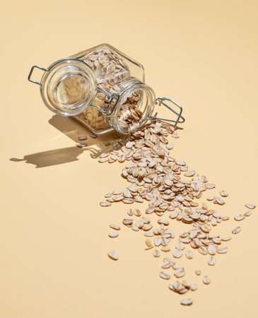 Oat flakes in a jar scattered on a yellow background. Healthy eating and wholesome diet breakfast concept. Advertising layout or banner for nutrition food.  Copy space.の写真素材