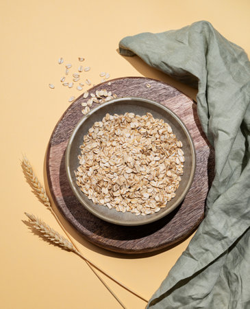 Oat flakes in bowl with wheat and napkin on a wooden board on a yellow background. Healthy eating and wholesome diet breakfast concept. Top view and copy space.の写真素材