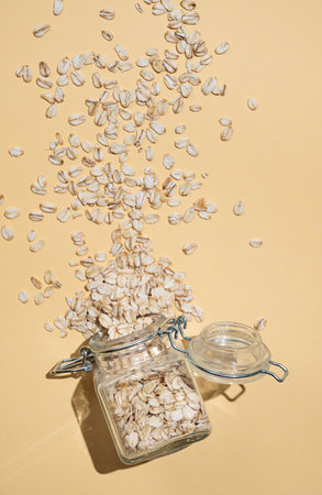 Oat flakes in a jar scattered on a yellow background. Healthy eating and wholesome diet breakfast concept. Advertising layout or banner for nutrition food.  Top view and copy space.の写真素材