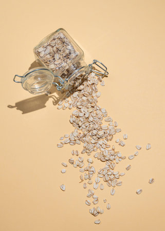 Oat flakes in a jar scattered on a yellow background. Healthy eating and wholesome diet breakfast...