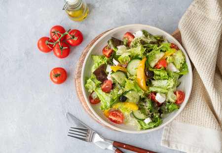 Healthy vegetable salad with lettuce, tomatoes, cucumbers, olives and feta cheese on light background. Fresh and natural diet food concept. Top view and copy space.の写真素材