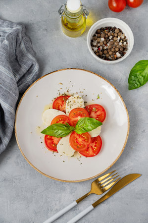 Caprese salad with sliced ââtomatoes, mozzarella and basil on a plate on a light background with fresh vegetables and olive oil. Healthy Mediterranean cuisine concept. Top view.の写真素材