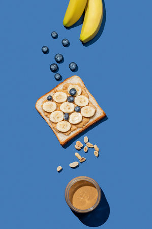 Peanut butter toast with banana, blueberry and nuts on a dark blue background. Concept of sweet and healthy snacks for advertising menu or banner. Top view and copy space.の写真素材
