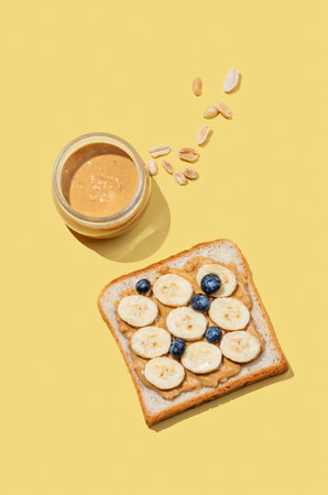 Peanut butter toast with banana, blueberry and nuts on a yellow background. Concept of sweet and healthy snacks for advertising menu or banner. Top view and copy space.の写真素材