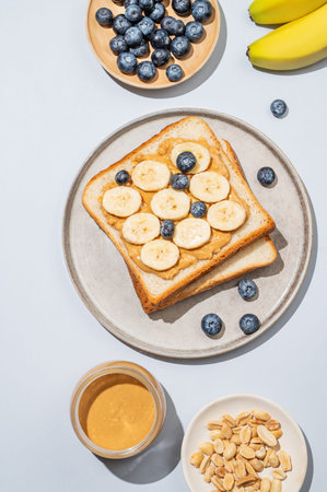 Peanut butter toast on a plate with banana, blueberry and nuts on a blue background. Concept of...