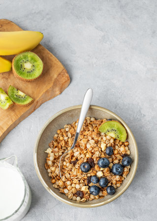 Homemade baked granola or muesli in a bowl with kiwi and blueberries on a light background with fresh fruits and milk. Healthy and nutritious breakfast concept. Top view and copy space.の写真素材