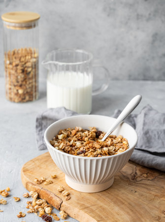 Homemade baked granola or muesli in a bowl on a wooden board on a light background with milk, baked oat flakes and spoon. Healthy and nutritious breakfast concept.の写真素材