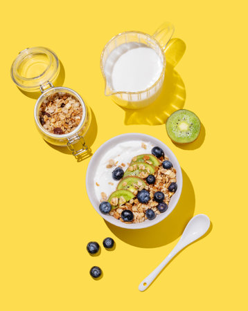 Natural yogurt with granola, kiwi and blueberries in a bowl on a bright yellow background. Healthy...