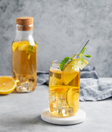 Iced drink with lemon and mint in a glass and bottle on a light background with shadows and citrus fruits. The concept of a cold tea or lemonade on a  summer day. Front view, copy space.の写真素材