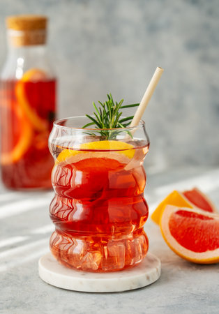 Refreshing cocktail with grapefruit, rosemary and ice in a glass on a table with bottle and natural light. Summer citrus drink or lemonade concept. Front view and copy space.の写真素材
