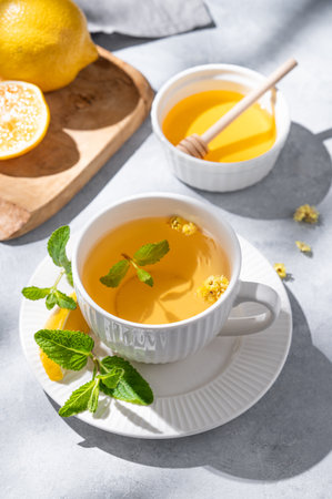Cup of herbal tea with lemon, honey and mint on light background with citrus fruits and morning shadows. Concept of healthy detox drink for breakfast.の写真素材