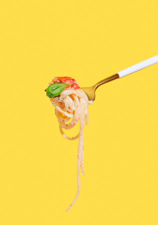 Fork with creamy spaghetti, tomato and basil on isolated bright yellow background. Italian or Mediterranean cuisine concept for menu banner or restaurant advertisement. Front view, copy space.の写真素材