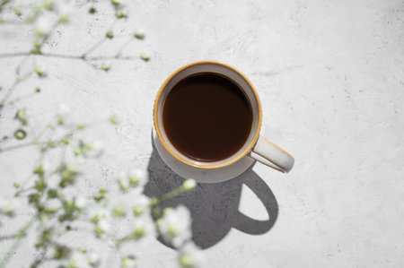 Cup of freshly brewed coffee and bouquet of gypsophila on light textured background with morning shadows. Aesthetic concept of breakfast drink. Top view and copy space.の写真素材