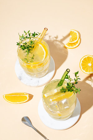 Two glasses of mocktail mojito with lemon, lime, thyme and ice. Citrus lemonade on a yellow background with fruits. Summer trendy cold drinks concept. Top view, copy space.の写真素材