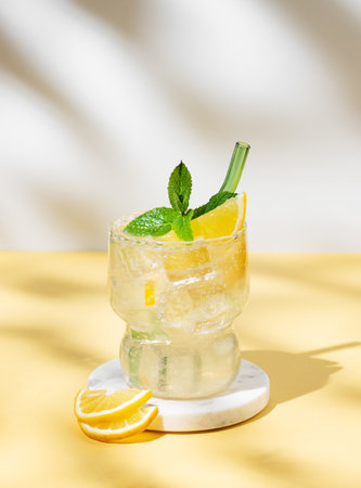 Fresh citrus mojito with lemon, mint and ice on a white yellow background with shadow. Summer trendy lemonade mocktail drink concept for bar menu or advertising. Front view, copy space.の写真素材