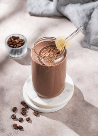 Vegetarian chocolate coffee smoothie with banana in a glass on a light  background with morning shadow. Healthy eating and detox diet concept for advertising menu or banner. Top view.の写真素材