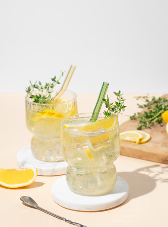 Two glasses of mocktail mojito with lemon, lime, thyme and ice. Citrus lemonade on a yellow background with fruits. Summer trendy cold drinks concept. Front view, copy space.の写真素材