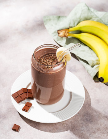 Vegetarian chocolate smoothie with banana in a glass on a light  background with fresh fruits and morning shadow. Healthy eating and detox diet concept. Top view.の写真素材