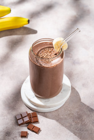 Vegetarian chocolate smoothie with banana in a glass on a light  background with morning shadow. Healthy eating and detox diet concept for advertising menu or banner. Top view.の写真素材