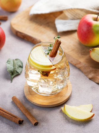 Chilled apple cocktail or cider in a glass with ice, garnished with cinnamon and thyme on a light background with slice of fruits. Refreshing drink concept.の写真素材