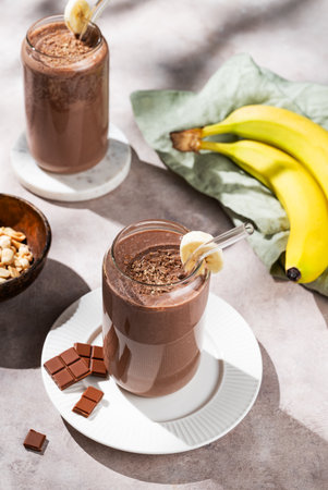 Vegetarian chocolate nuts smoothie with banana in a glass on a light  background with fresh fruits and morning shadow. Healthy eating and detox diet concept. Top view.の写真素材