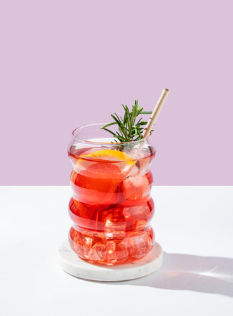 Refreshing mocktail with grapefruit, rosemary and ice in a glass on a white pink background with shadows. Summer citrus drink or lemonade concept for cafe menu advertising banner. Front viewの写真素材