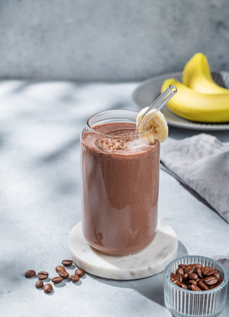Chocolate smoothie with banana and coffee in a glass on a light  background with morning shadow. Healthy eating and detox diet concept for advertising menu or banner.の写真素材