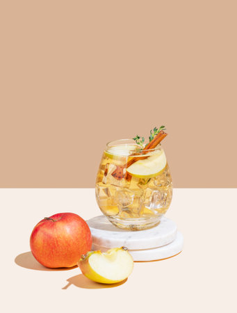 Apple cocktail or cider in a glass with ice, cinnamon and thyme, on a marble stand on a white beige background. Refreshing drink concept for advertising or bar menu banner. Front view, copy spaceの写真素材
