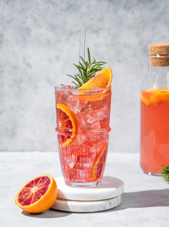 Blood orange cocktail with ice and rosemary on a marble stand on a gray background with bottle. Summer citrus drink concept for cafe menu advertising banner. Front view, copy space.の写真素材