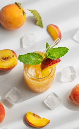 Refreshing peach cocktail, lemonade or iced tea on a white table with shadows, ice cubes and fruits. Concept of a cold alcoholic or non-alcoholic summer drink with mint and fresh fruits. Top view.の写真素材