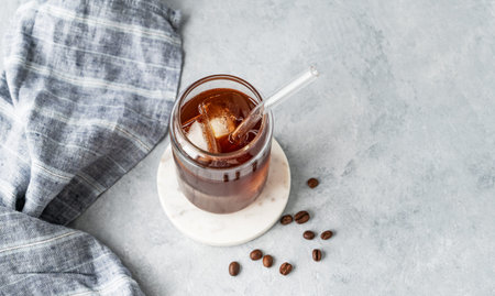 Cold brew coffee in a glass with ice on a marble stand on a light concrete background with coffee...