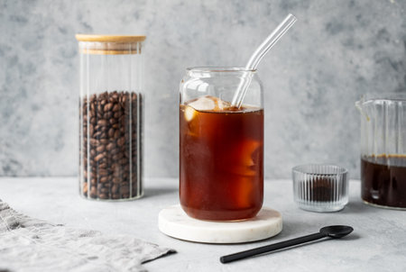 Cold brew coffee in a glass with ice on a marble stand on a light background with coffee beans and...