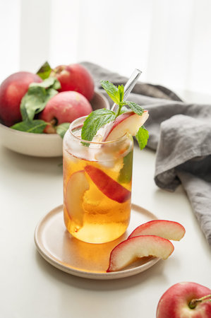 Ice tea with peach, mint in a glass on a white table near window with fresh fruits, napkin and sunlight. Refreshing summer drink concept for bar or cafe menu. Front view, copy space.の写真素材