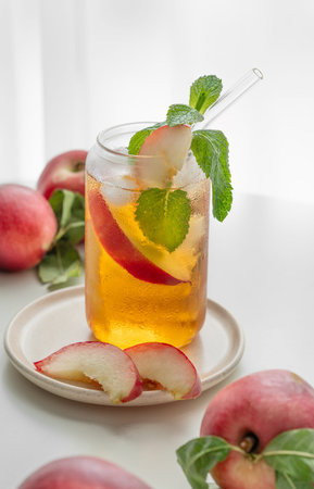 Ice tea with peach, mint in a glass on a white table near window with fresh fruits and sunlight close up. Refreshing summer drink concept for bar or cafe menu. Front view, copy space.の写真素材