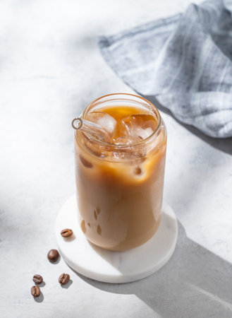 Ice latte coffee in a glass with milk on a light background with coffee beans and morning shadows. Trendy summer craft refreshing drink concept. Top view, copy space.の写真素材