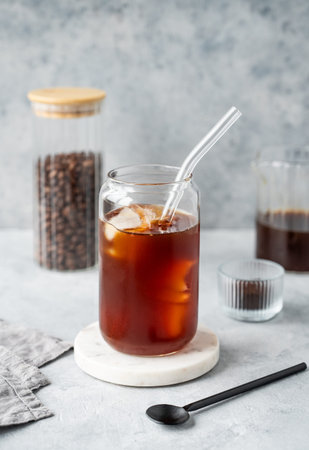 Cold brew coffee in a glass with ice on a marble stand on a light concrete background with coffee...