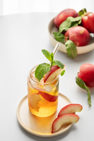 Ice tea with peach, mint in a glass on a white table near window with fresh fruits and sunlight....