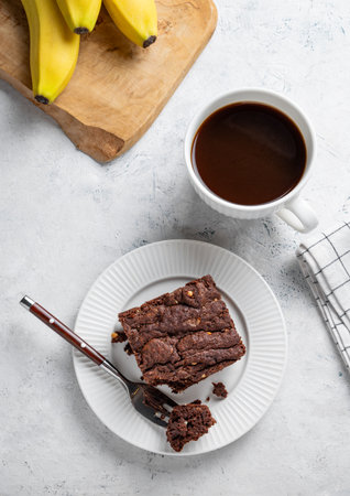 Vegetarian chocolate banana brownie on a plate on a light background with a cup of freshly brewed coffee and fresh fruits. The concept of homemade dietary gluten-free baking. Top view, copy space.の写真素材
