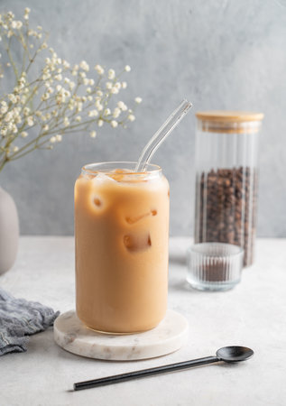 Ice latte coffee in a glass with milk on a marble board on a  light background with coffee beans and bouquet of gypsophila. Trendy summer craft refreshing drink concept. Front view, copy space.の写真素材