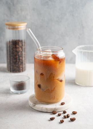 Ice latte coffee in a glass with milk on a marble board on a  light background with coffee beans. Trendy summer craft refreshing drink concept. Front view, copy space.の写真素材