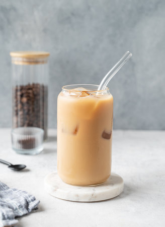 Ice latte coffee in a glass with milk on a marble board on a  light background with coffee beans and spoon. Trendy summer craft refreshing drink concept. Front view, copy space.の写真素材