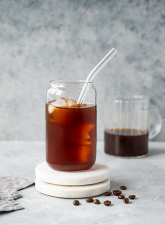 Cold brew coffee in a glass with ice on a marble stand on a light concrete background with coffee beans. Trendy summer craft refreshing drink. Front view, copy space.の写真素材