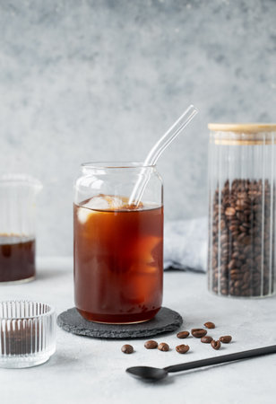 Cold brew coffee in a glass with ice on a light concrete background with coffee beans and spoon. Trendy summer craft refreshing drink. Front view, copy space.の写真素材