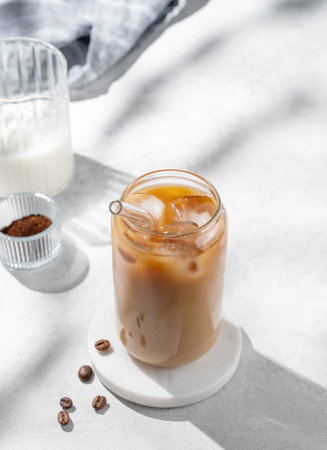 Ice latte coffee in a glass with milk on a light background with coffee beans and morning shadows. Trendy summer craft refreshing drink concept. Top view, copy space.の写真素材