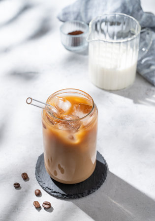 Ice latte coffee in a glass with milk on a light background with coffee beans and morning shadows. Trendy summer craft refreshing drink concept. Top view, copy space.の写真素材