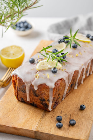 Homemade blueberry lemon loaf cake on a wooden board on a light background with fresh berries, herbs...