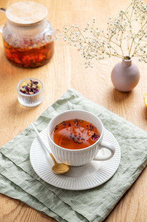 A cup of herbal tea with lemon and bouquet of flowers on a wooden table with teapot and napkin. Morning detox drink concept for breakfast. Top view.の写真素材