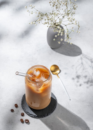 Ice latte coffee in a glass with milk on a white background with bouquet of flowers, coffee beans...